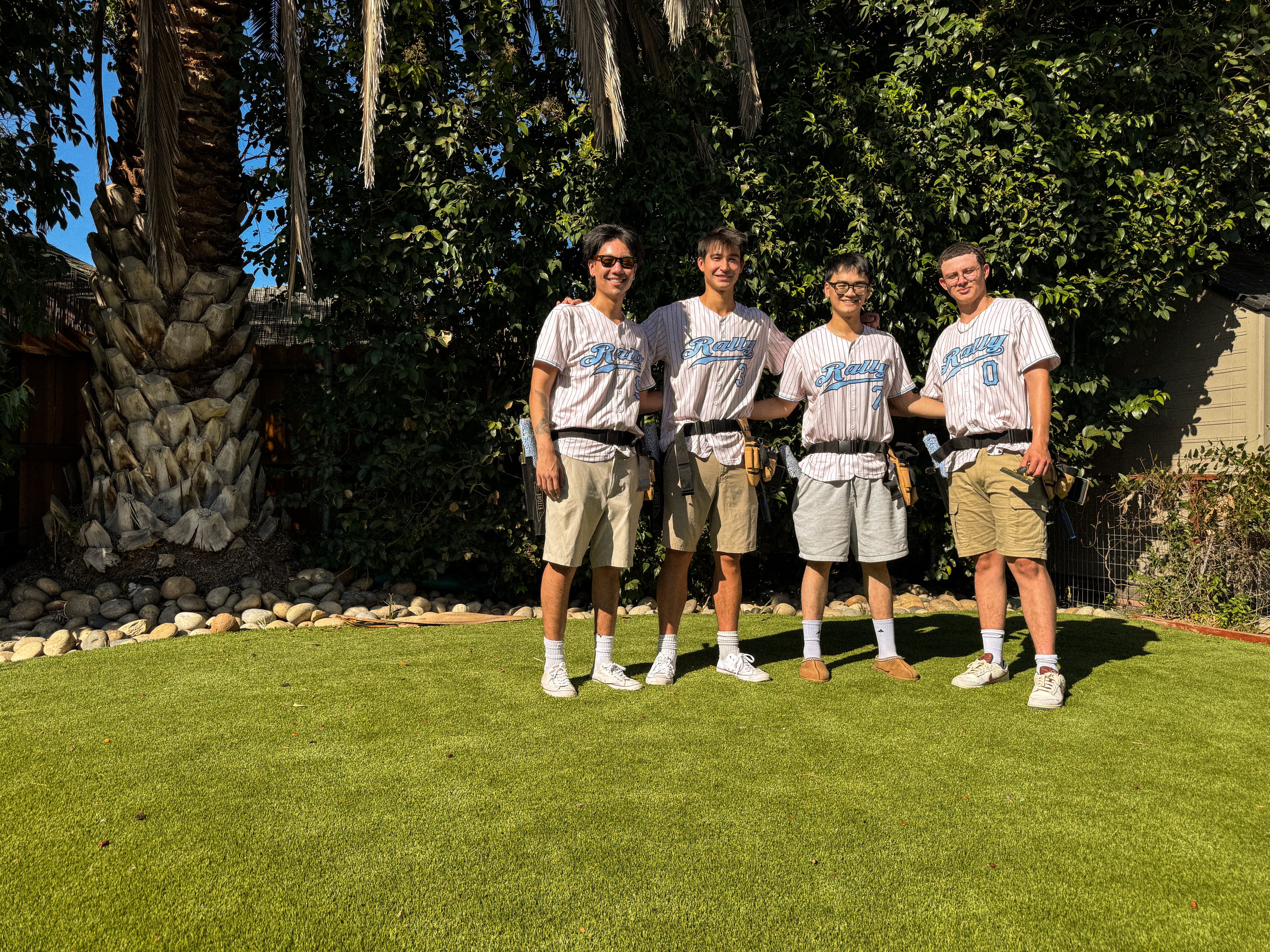 The 4 Rally founders standing together on a lawn in pinstriped Rally jerseys and tool belts.