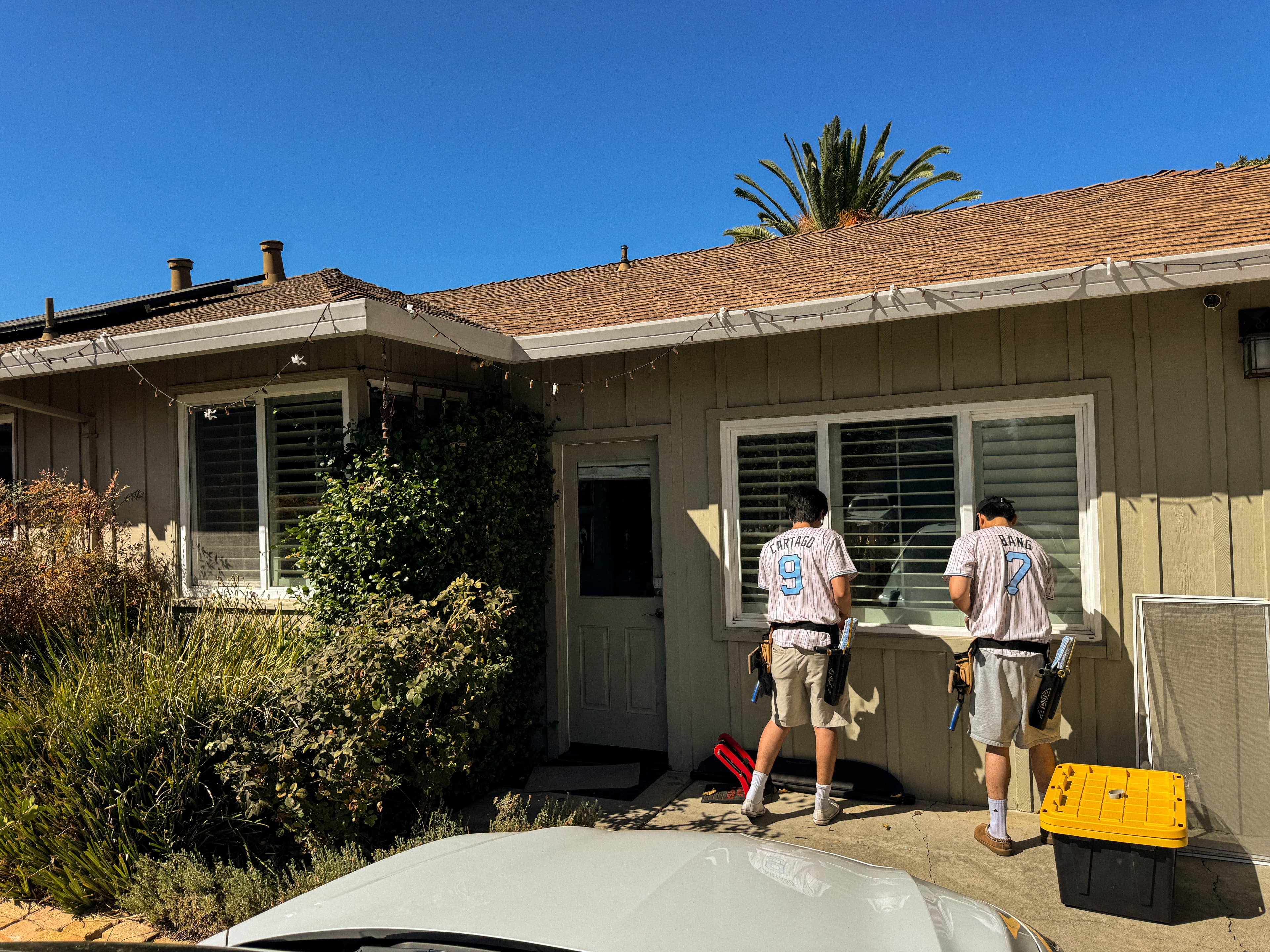Two Rally cleaners in jerseys and tool belts washing exterior windows at a single-story home, squeegees in hand.