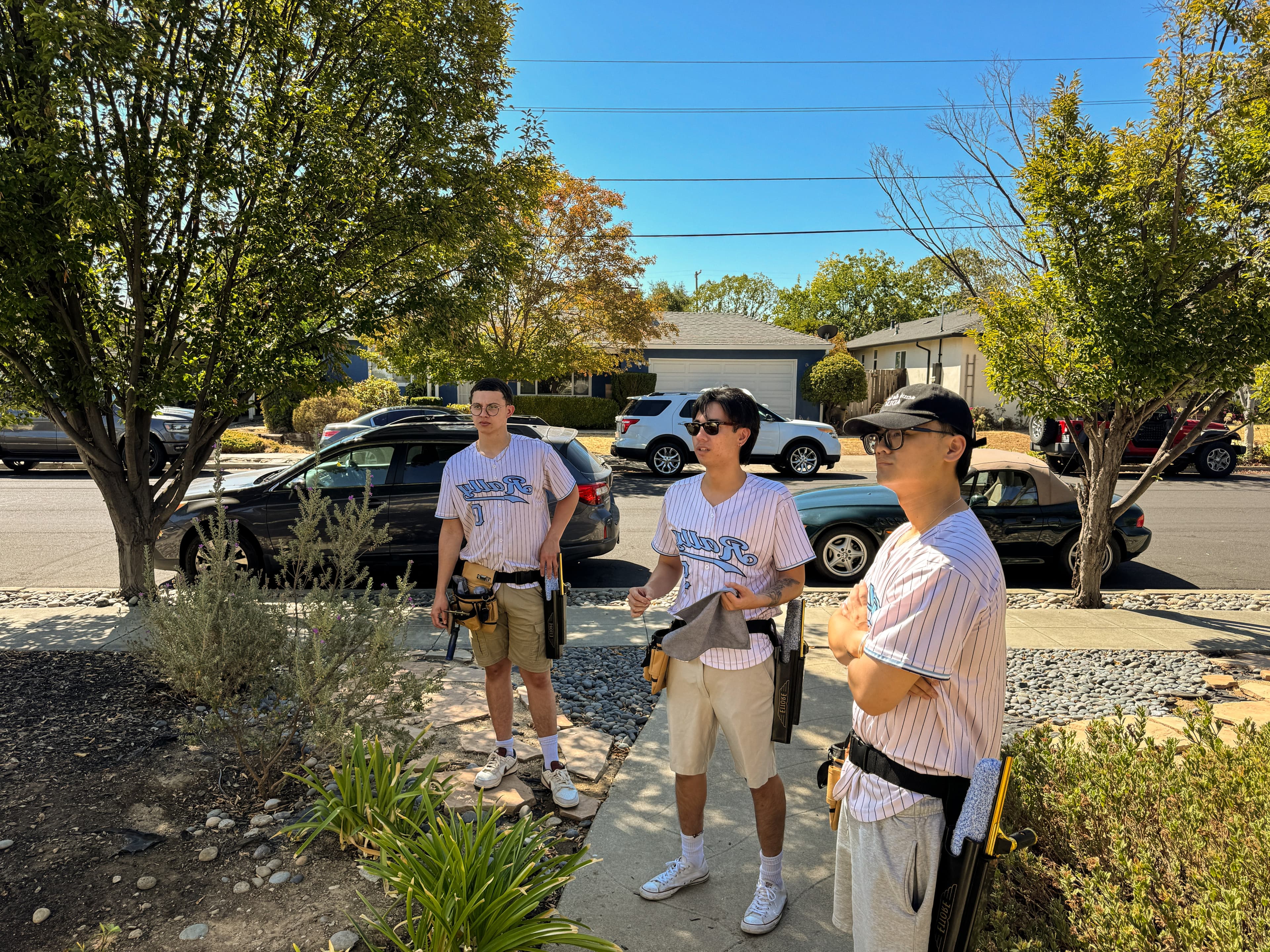Three of the Rally crew in jerseys and tool belts standing on a residential street, looking up at a house.